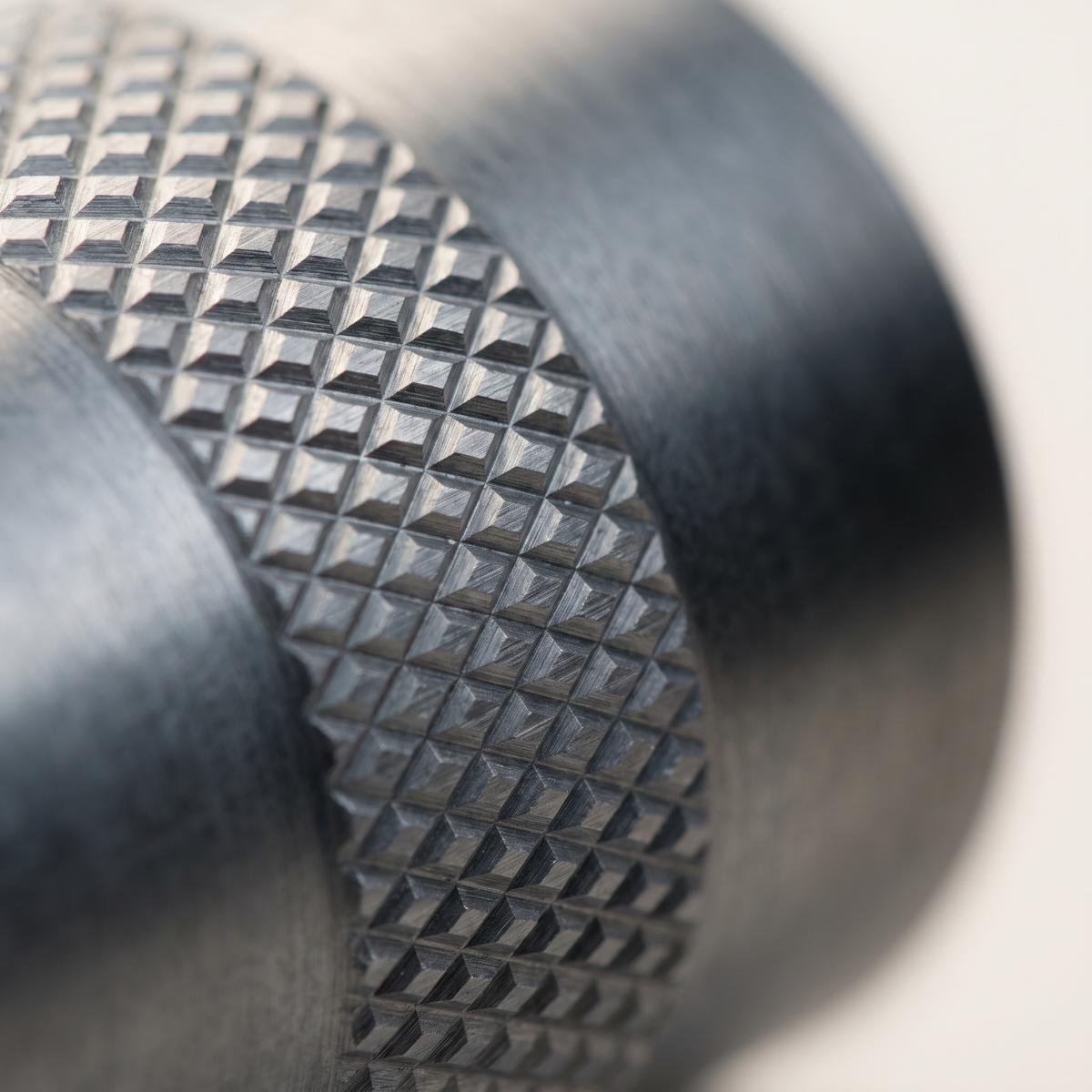 Macro view of an even diamond knurl cut into a metal cylinder under raking light.
